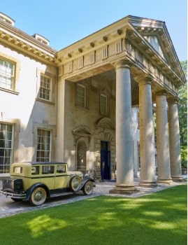Elegant historic mansion with large columns and a vintage car parked at the entrance.