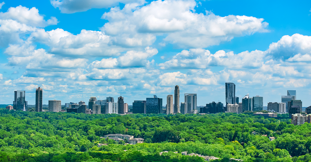 Buckhead Atlanta skyline rising above a dense green forest under a bright blue sky.