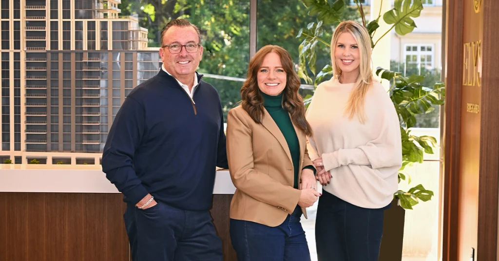 Three sales team members stand beside a scale model of a residential building inside a showroom.