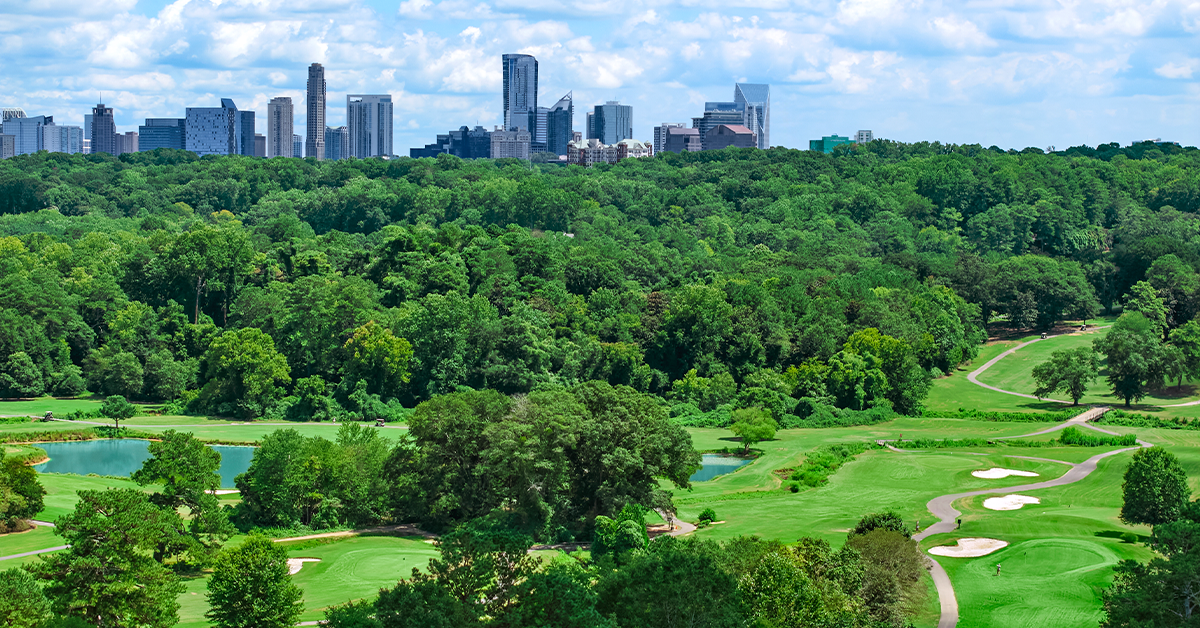 Green golf course with sand bunkers and city skyline in distance.