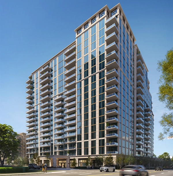Street-level view of a glass high-rise condo tower with balconies, cars, and a clear blue sky
