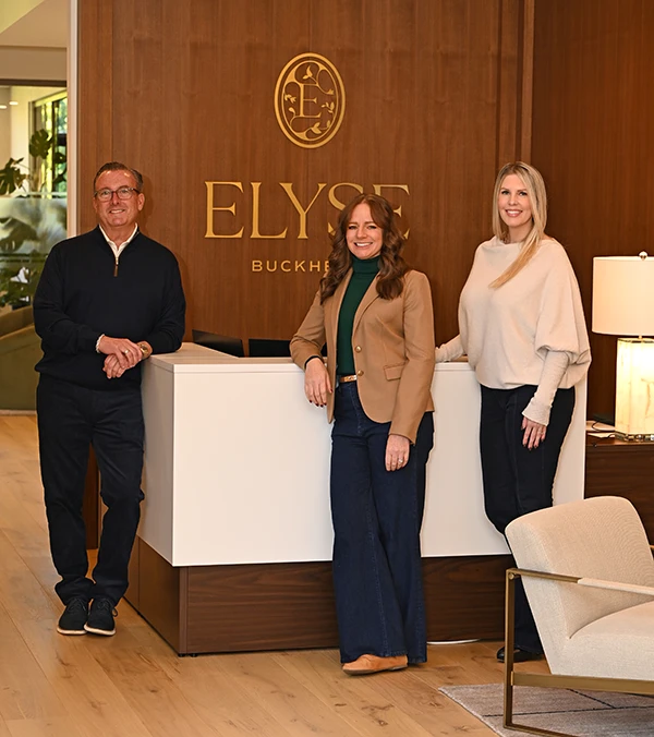 Three people standing in a lobby in front of Elyse Buckhead logo wall