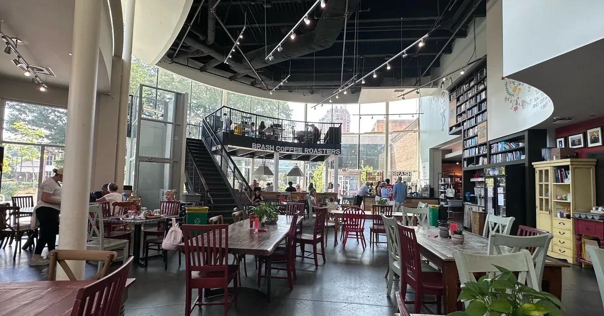 Brash Coffee Roasters' spacious two-story café features eclectic mismatched seating, floor-to-ceiling windows, and an industrial-chic design with an adjacent...